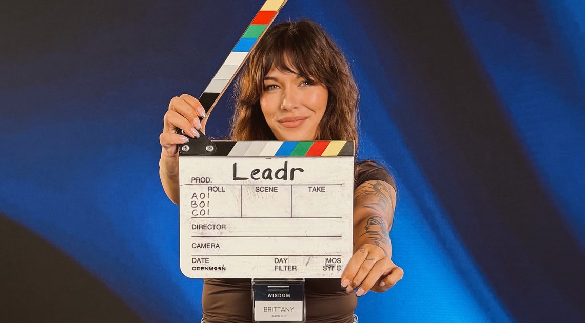 Brittany Beltz holding a LEADR clapperboard on a studio backdrop